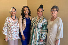 Four women stand together, smiling.